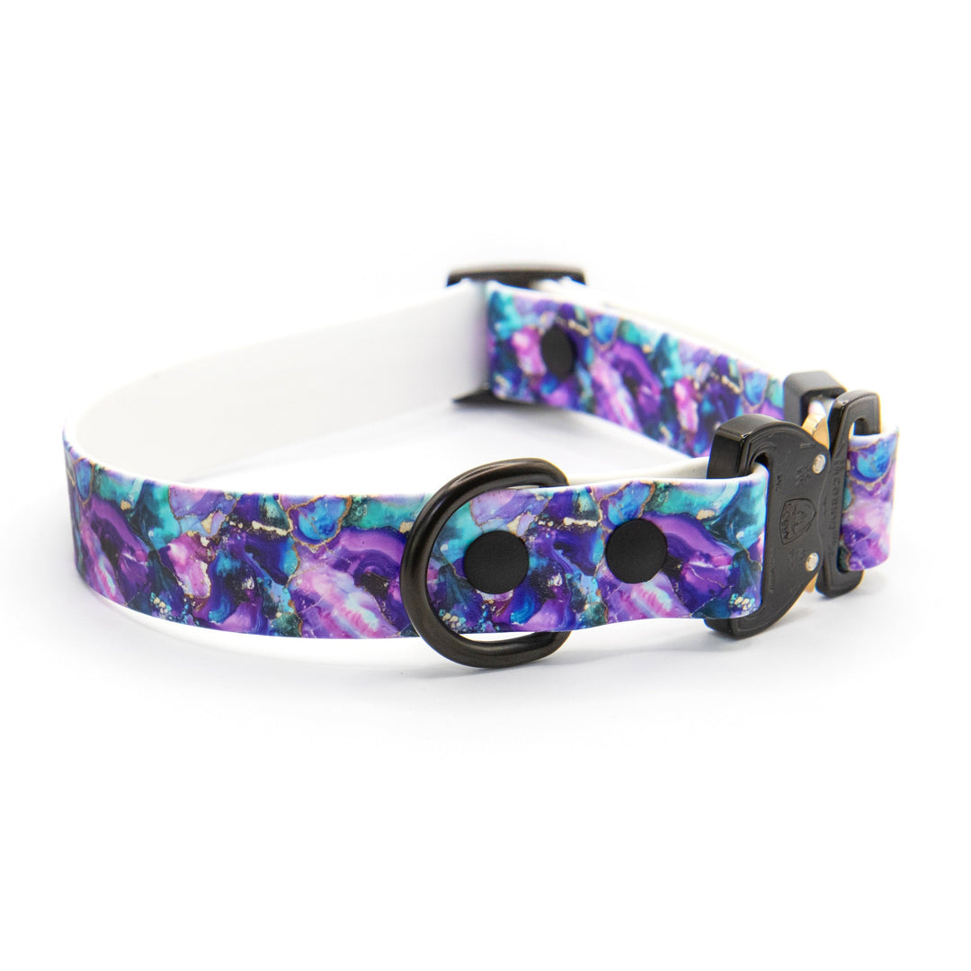 A dog collar with a vibrant purple, blue, and teal galaxy print, featuring a black metal ring and a black plastic buckle, displayed on a clean white background.