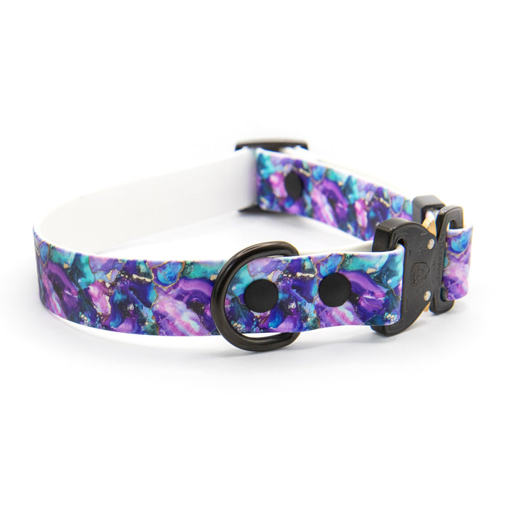A dog collar with a vibrant purple, blue, and teal galaxy print, featuring a black metal ring and a black plastic buckle, displayed on a clean white background.
