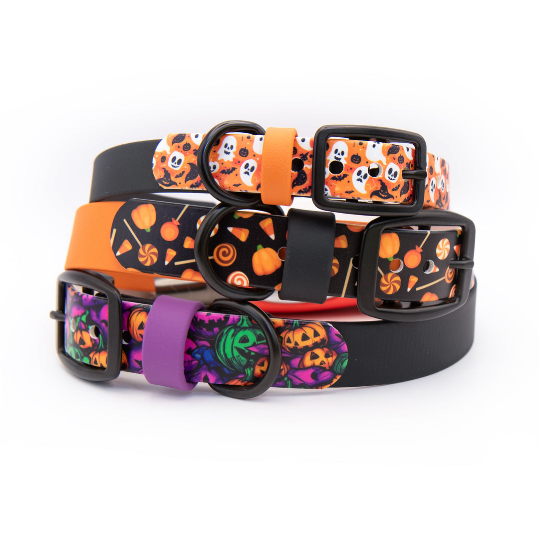 Three Halloween-themed dog collars stacked together on a white background. The top collar is black with an orange skull and candy print.
