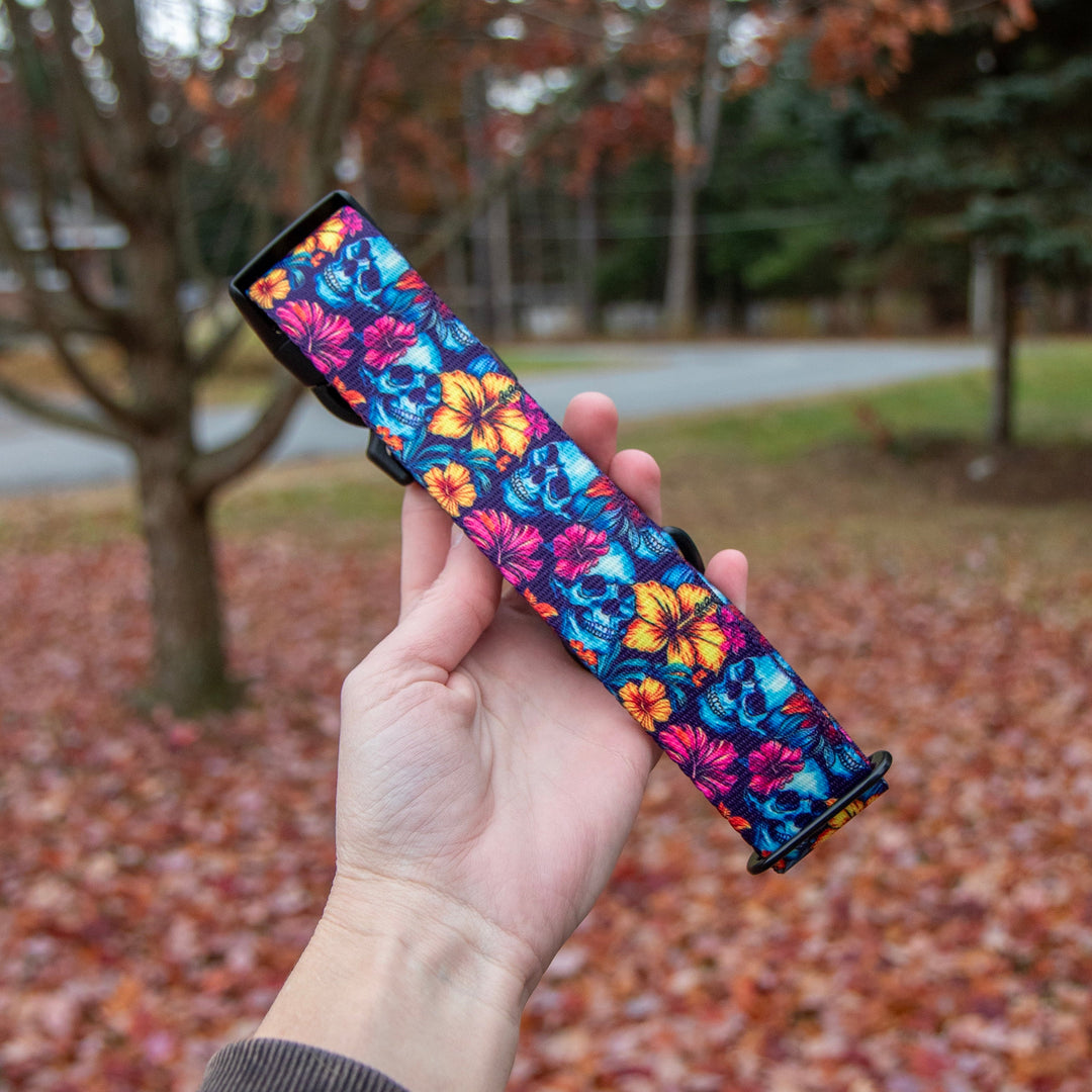 Hand holding a colorful floral-patterned object against a background of trees with autumn leaves.