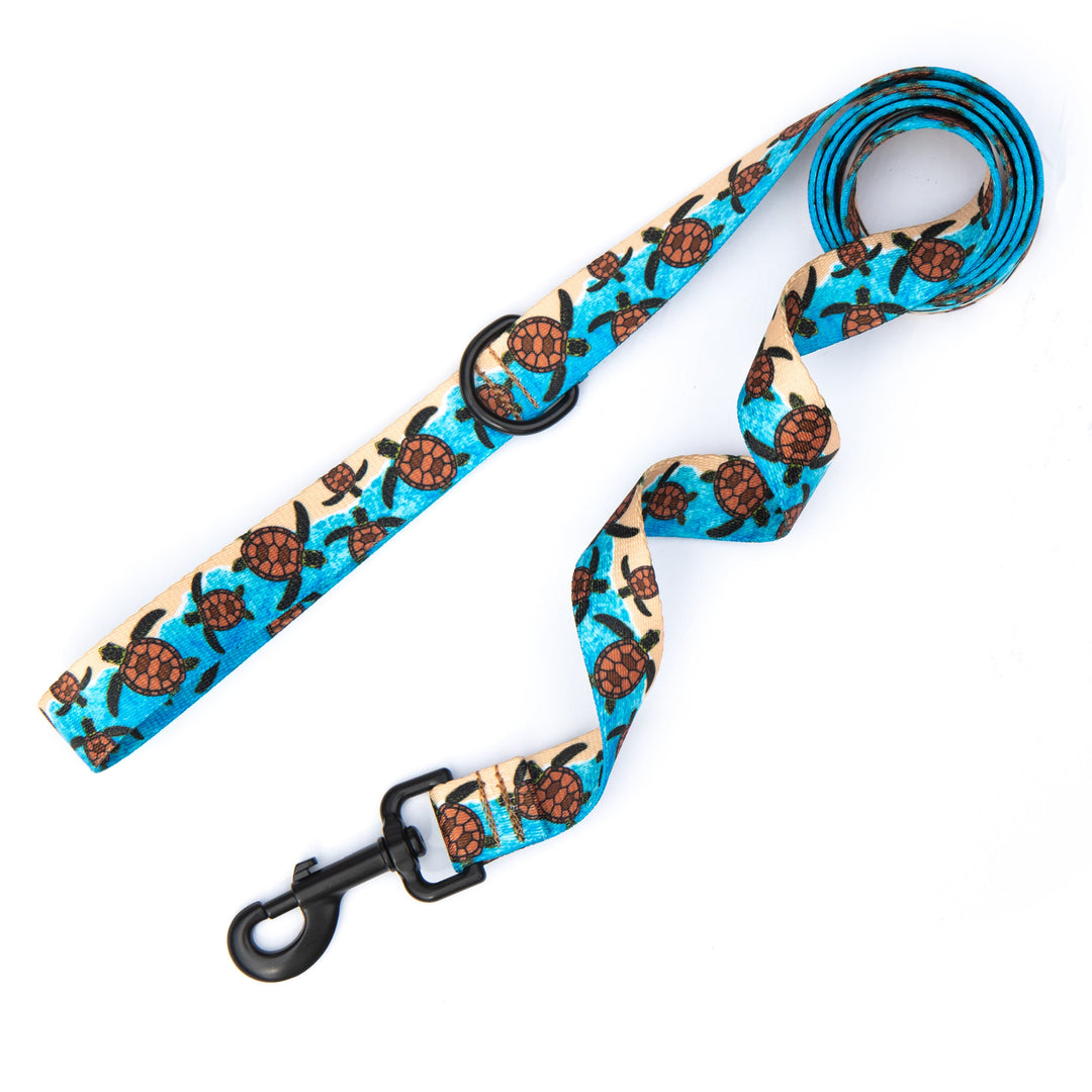 A pet leash with a repeating sea turtle pattern on a bright turquoise blue background, featuring black hardware including a swivel clasp and metal ring.